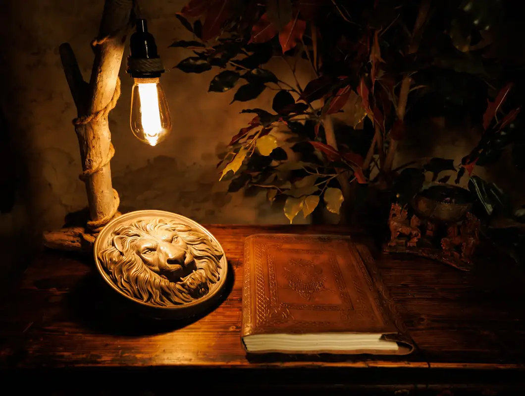 A carved lion's head and a leather-bound book under a lamp in Beaver's Den